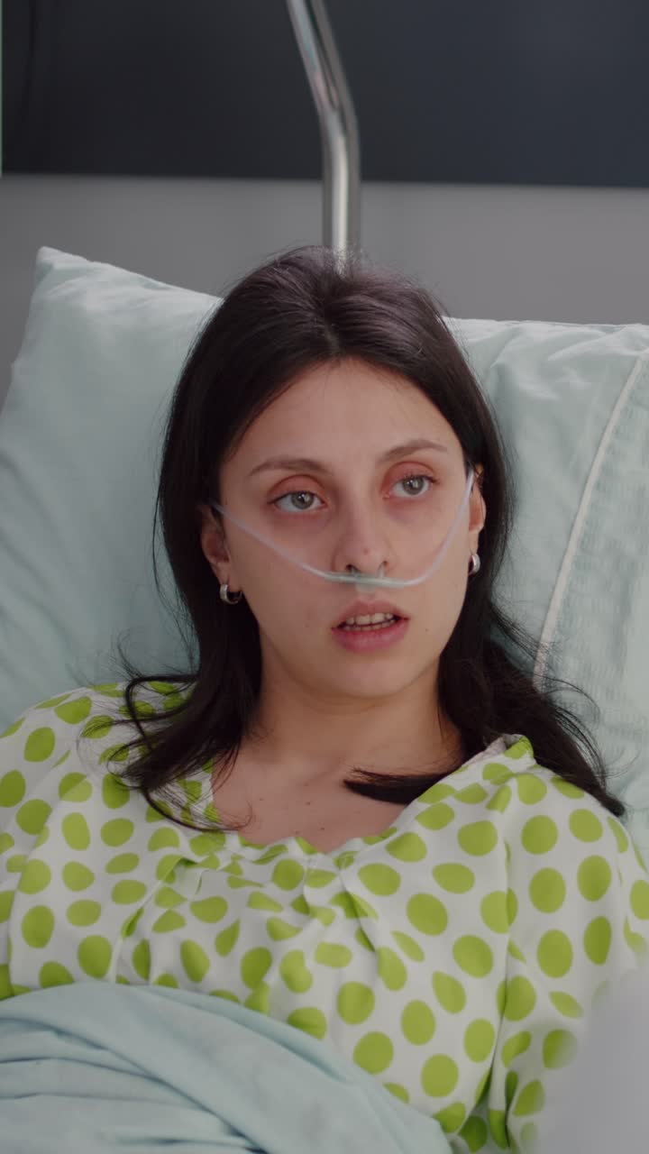 Vertical video: Closeup of sick woman with nasal oxygen tube resting in bed