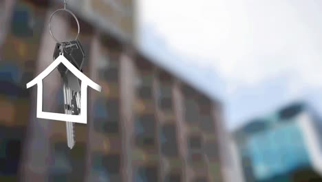 Animation-of-silver-house-key-fob-and-key,-hanging-in-front-of-blurred-city-building