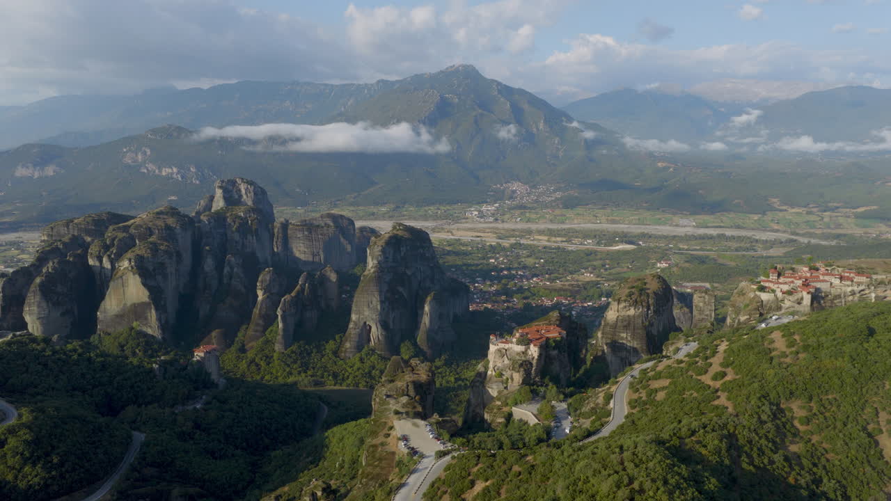 Cinematic aerial view of Meteora monastery in Greece perched on towering cliffs, dramatic rock formations and lush green valley create a breathtaking historic scene