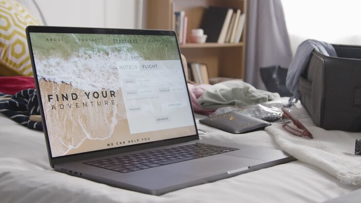 Åben kuffert på seng derhjemme, der pakkes til sommerferien, med bærbar computer, der viser bookingdetaljer for fly og hotel