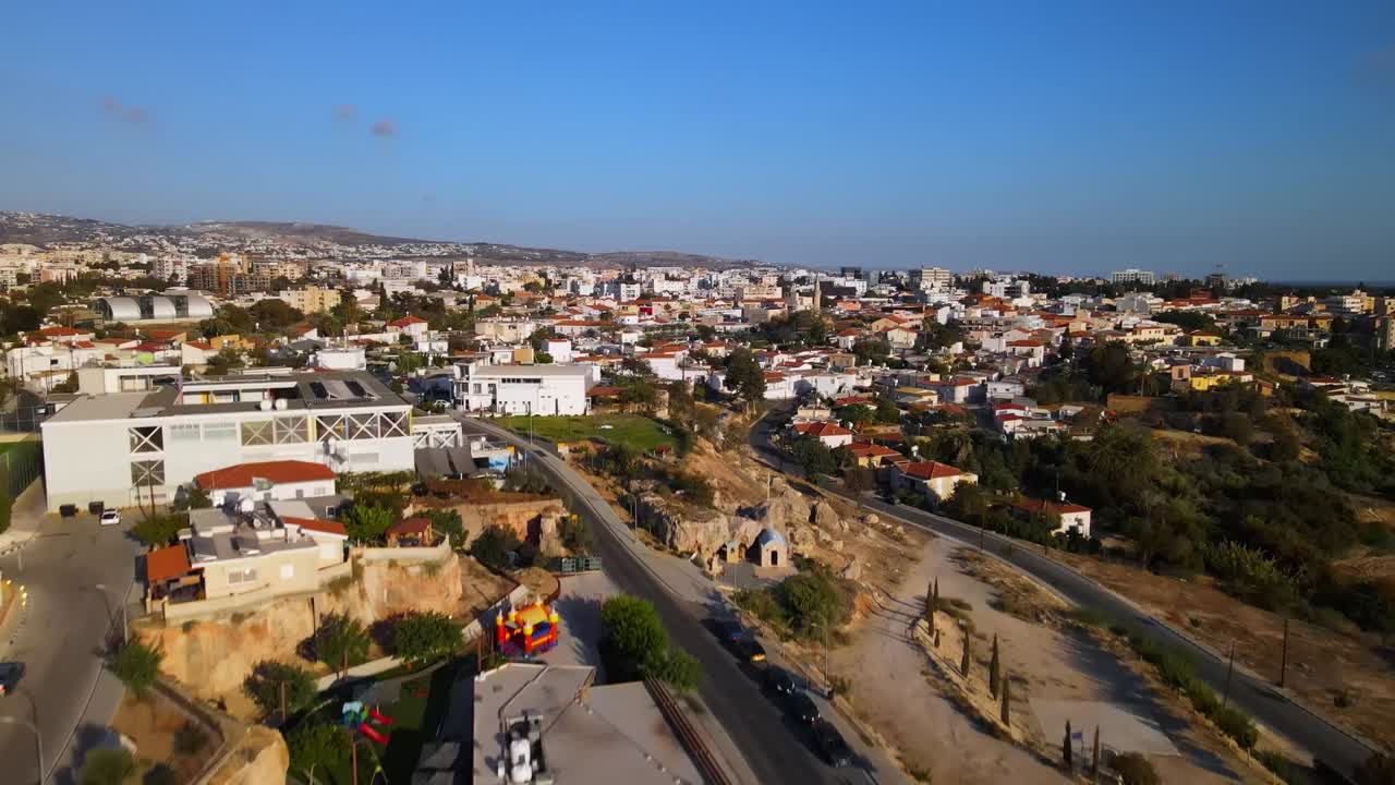 Aerial view over a suburban district in Naples, Italy—showing hillside housing, winding roads, and a circular park, with Mediterranean architecture under a clear blue summer sky