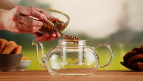 person brewing herbal tea in a glass teapot