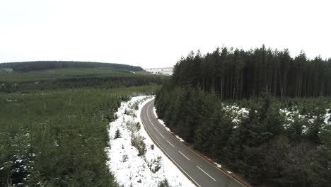 Snowy-curved-winter-woodland-road-aerial-tracking-forward-view-following-forest-tree-landscape