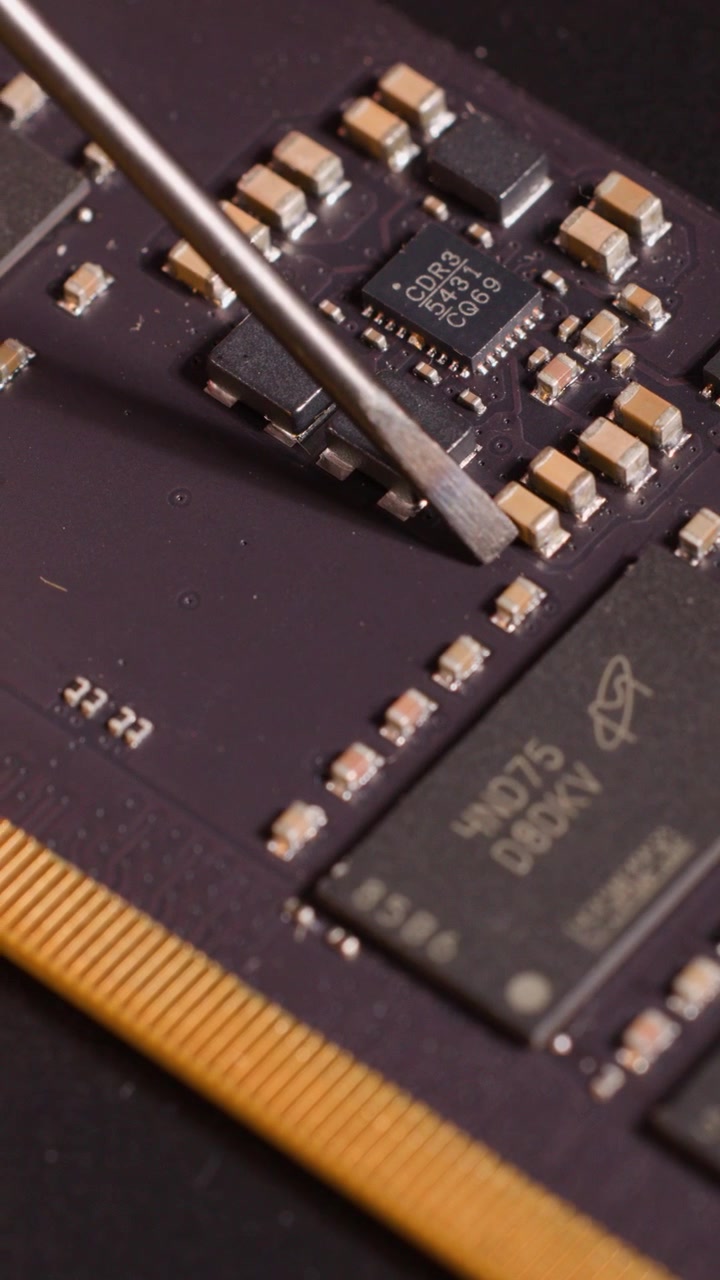 A metal tool inspects electronic components on a motherboard during a macro close-up shot