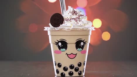 kawaii bubble tea adorned with whipped cream, chocolate cookie, colorful sprinkles, resting in transparent plastic cup against blurred background