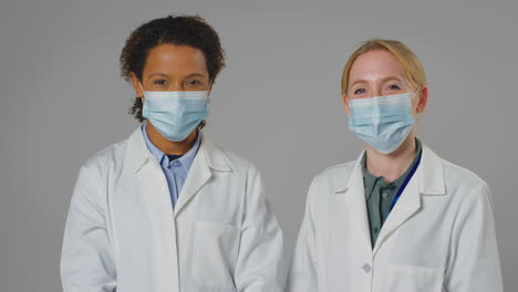 studio portrait of two female doctors or lab workers wearing face masks in white coats