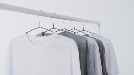 video of white and grey t shirts on hangers and copy space on white background