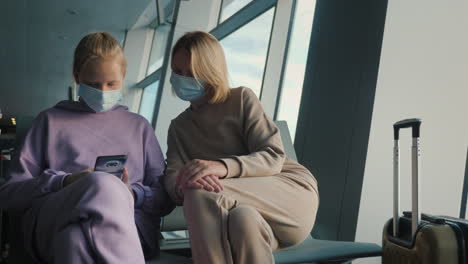 a woman with a child is waiting for a flight in the airport terminal. they are wearing protective masks to prevent infection with coronavirus.