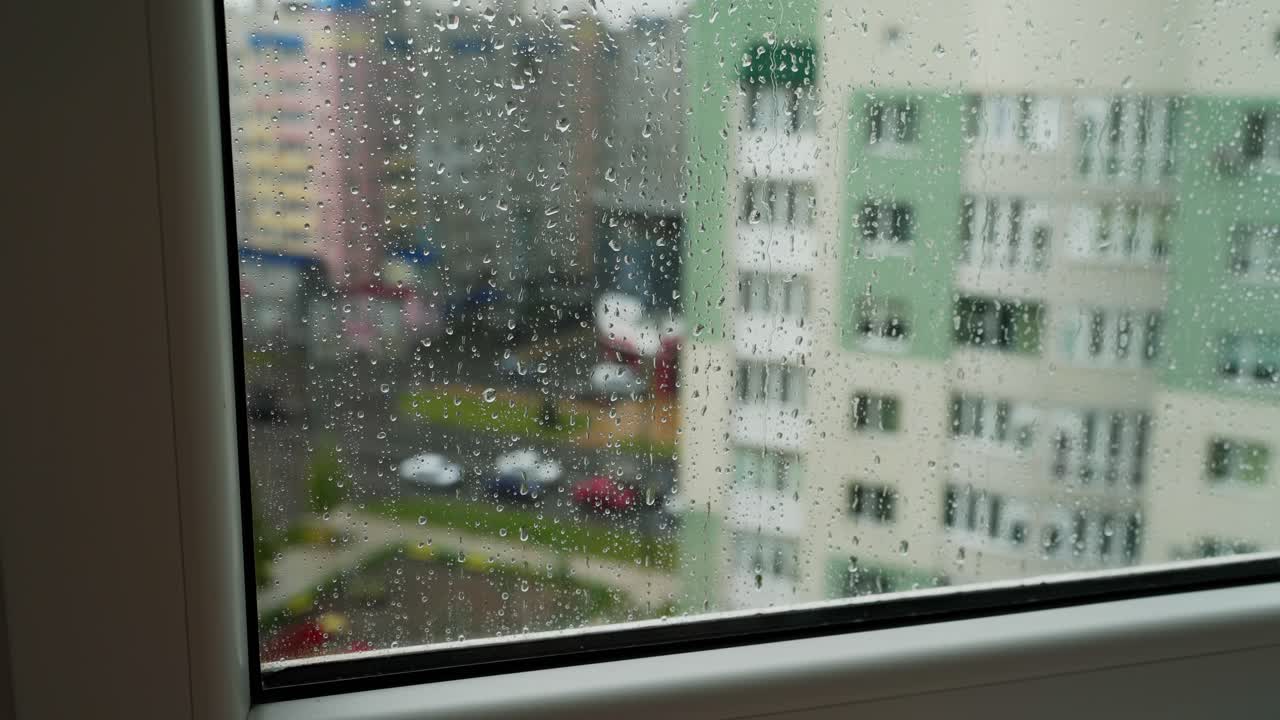 Rain drops on window glass in viewing cityscape. Drops of rain on a window pane with buildings background. Raining scenery on window.