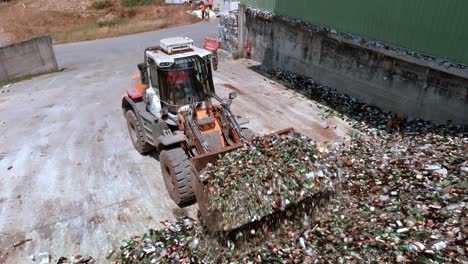 la excavadora de carretilla está agarrando vidrio en el almacén y quitándolo, la máquina de servicio pesado tiene un brazo largo equipado con un accesorio para agarrar vidrio, vista de dron, concepto de reciclaje de vidrio