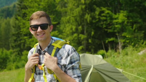 a young man with a backpack is looking at the camera standing in the background of a camping tent po