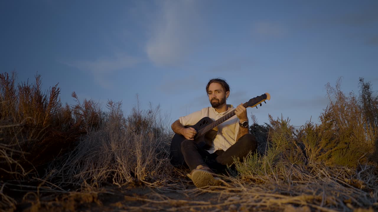 Mand spiller guitar udendørs ved solnedgang