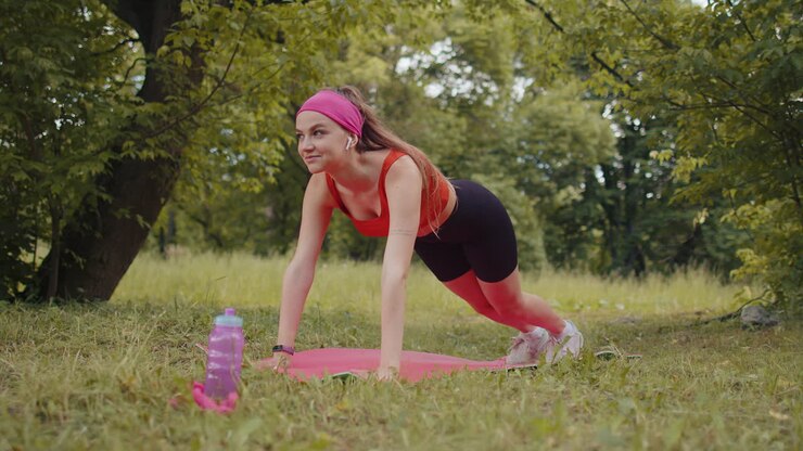 Athletic sporty fit girl doing workout in park on sport mat performing training yoga, plank pose