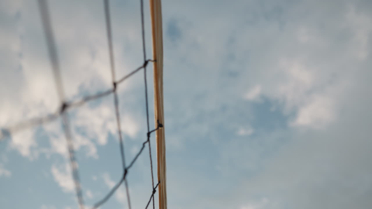 primer plano dinámico de una red de voleibol con la pelota volando sobre ella contra un cielo azul brillante, captura un momento lleno de acción de un juego de voleobol al aire libre, destacando el movimiento
