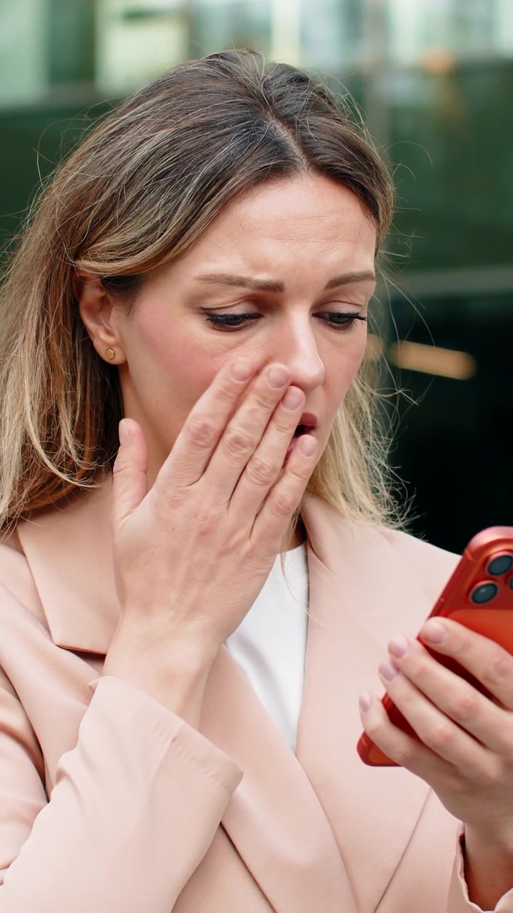 Young woman upset walking in city street reading bad smartphone message near modern business center