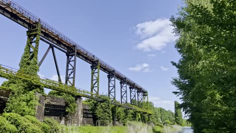 Von-Der-Natur-übernommenes-Und-Bewachsenes-Metallgerüst-Im-Landschaftspark-Duisburg-Nord-An-Einem-Fluss