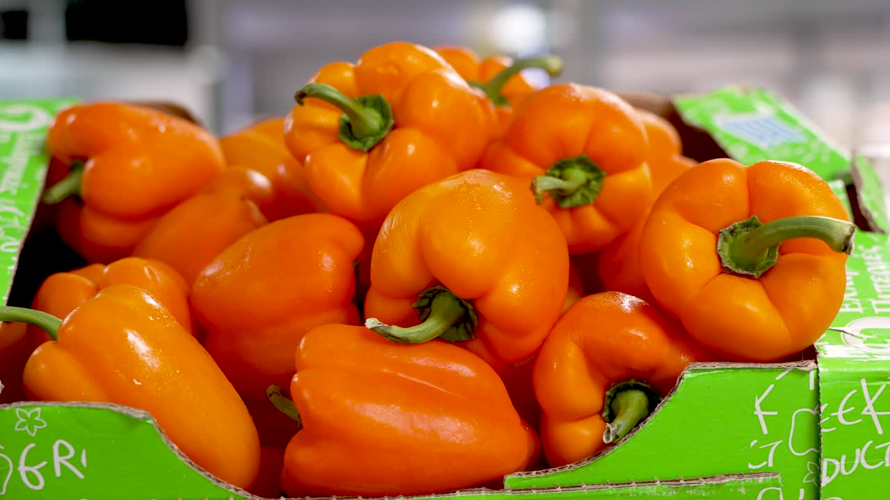 Bright orange bell peppers fill a cardboard box at a bustling local market. Shoppers are drawn to the vivid colors and fresh produce, ready to enhance their meals with these nutritious vegetables