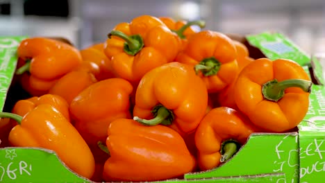 bright orange bell peppers fill a cardboard box at a bustling local market. shoppers are drawn to the vivid colors and fresh produce, ready to enhance their meals with these nutritious vegetables