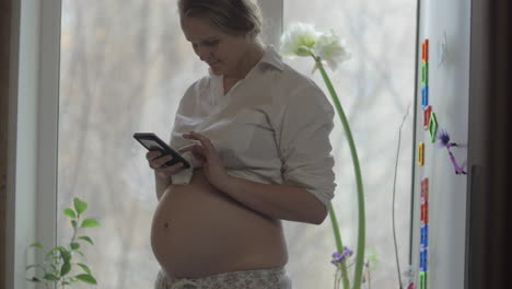 Smiling-pregnant-woman-with-mobile-phone-at-home