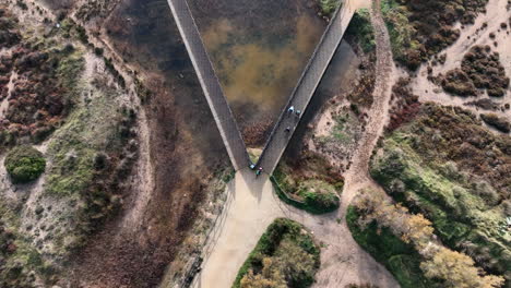 Aerial-view-looking-down-at-cyclists-riding-across-wooden-autumn-marshland-nature-reserve-boardwalk