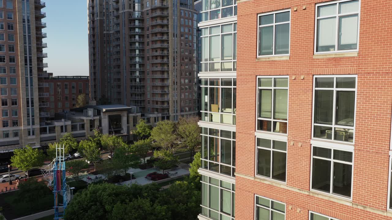 การลงจากอากาศผ่านย่านใจกลางเมือง Reston รัฐเวอร์จิเนีย ที่มีอาคารสำนักงานทันสมัยและส่วนหน้าอาคารกระจก สภาพแวดล้อมเมืองที่สว่างไสวด้วยแสงแดดล้อมรอบด้วยต้นไม้ จัดแสดงสถาปัตยกรรมร่วมสมัยในธุรกิจที่มีชีวิตชีวา