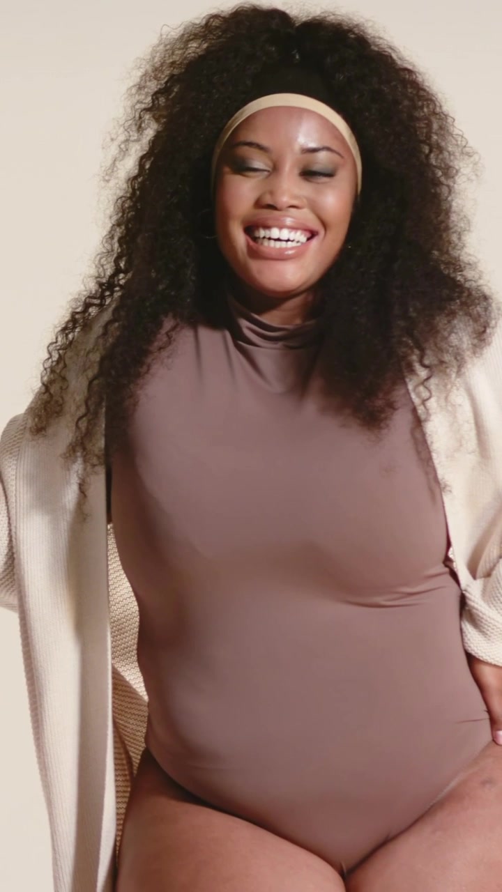 Vertikal video: Smilende model i bodysuit og cardigan justerer sin cardigan i et studie under en optagelse.