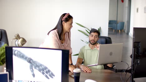 discussing robotic arm design, colleagues collaborating using laptop in office