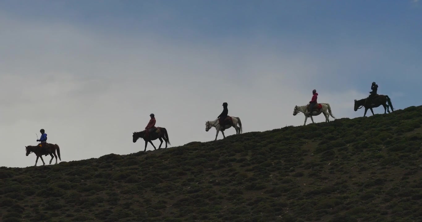Una ripresa aerea cinematografica con movimento laterale cattura il movimento silenzioso di cavalieri contro un cielo cupo e poco illuminato mentre percorrono un pendio collinare oscurato a Mustang, Nepal