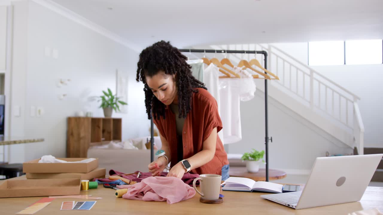Donna adulta che indossa una sovracamicia color ruggine mentre sistema un capo d'abbigliamento rosa su un tavolo da lavoro in legno in un luminoso studio casalingo