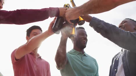 happy diverse male friends talking and drinking beer in garden on sunny day