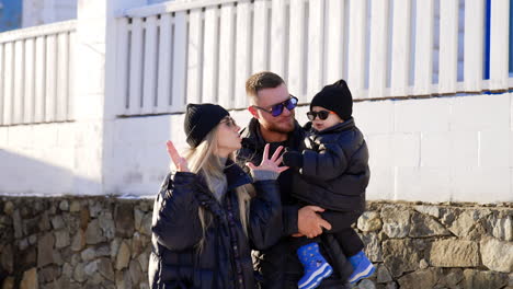 modern caucasian family with little baby wearing warm clothes and sunglasses. mom plays with a child trying to entertain him.