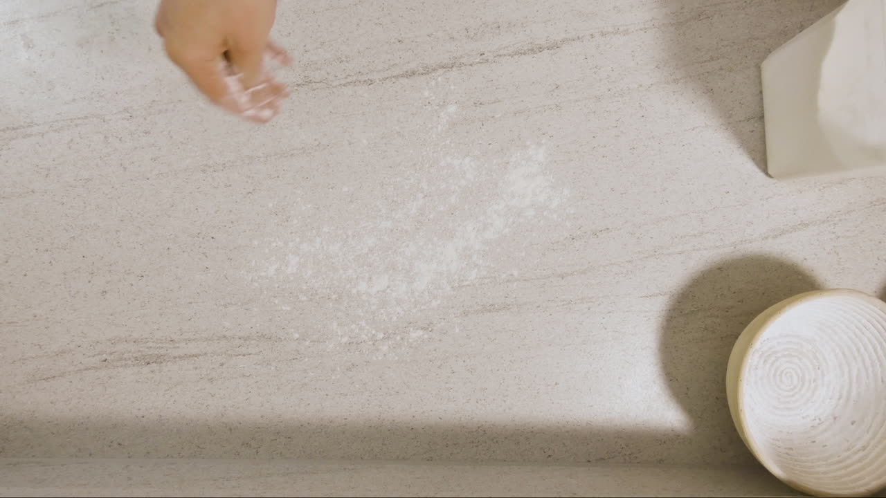 Toma cenital de un joven chef dando forma a masa madre en una encimera de cocina y colocándola en una cesta para hornear, lista para meter al horno