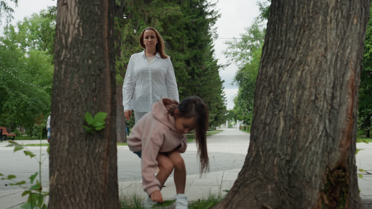 Witte moeder en dochter lopen langs een met bomen omzoomd pad, moeder begeleidt nieuwsgierige dochter terwijl ze door een zomerpark wandelen, casual kleding met roze hoodie en witte blouse, warme liefdevolle glimlachen