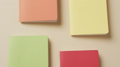 Overhead-view-of-colourful-notebooks-arranged-on-beige-background,-in-slow-motion