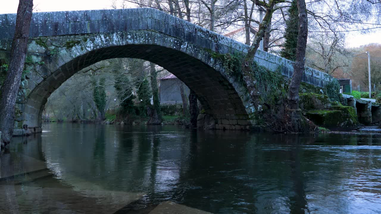 Flowing water rushes below Roman arched bridge with shallow water steps on edge