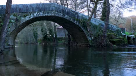 el agua que fluye corre por debajo del puente arqueado romano con escalones de agua poco profundos en el borde