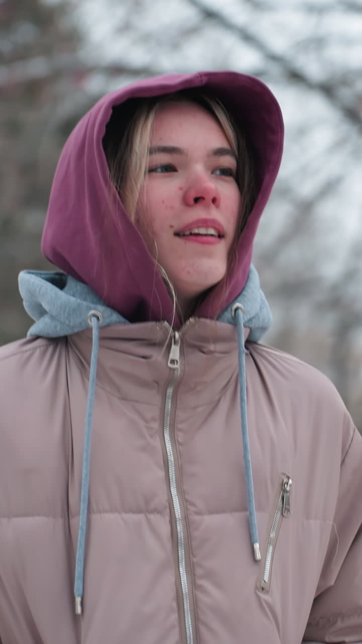 dama corriendo en el parque de invierno frío con expresión facial reflexiva, vestida con una capucha y abrigo cálido, árboles cubiertos de nieve en el fondo