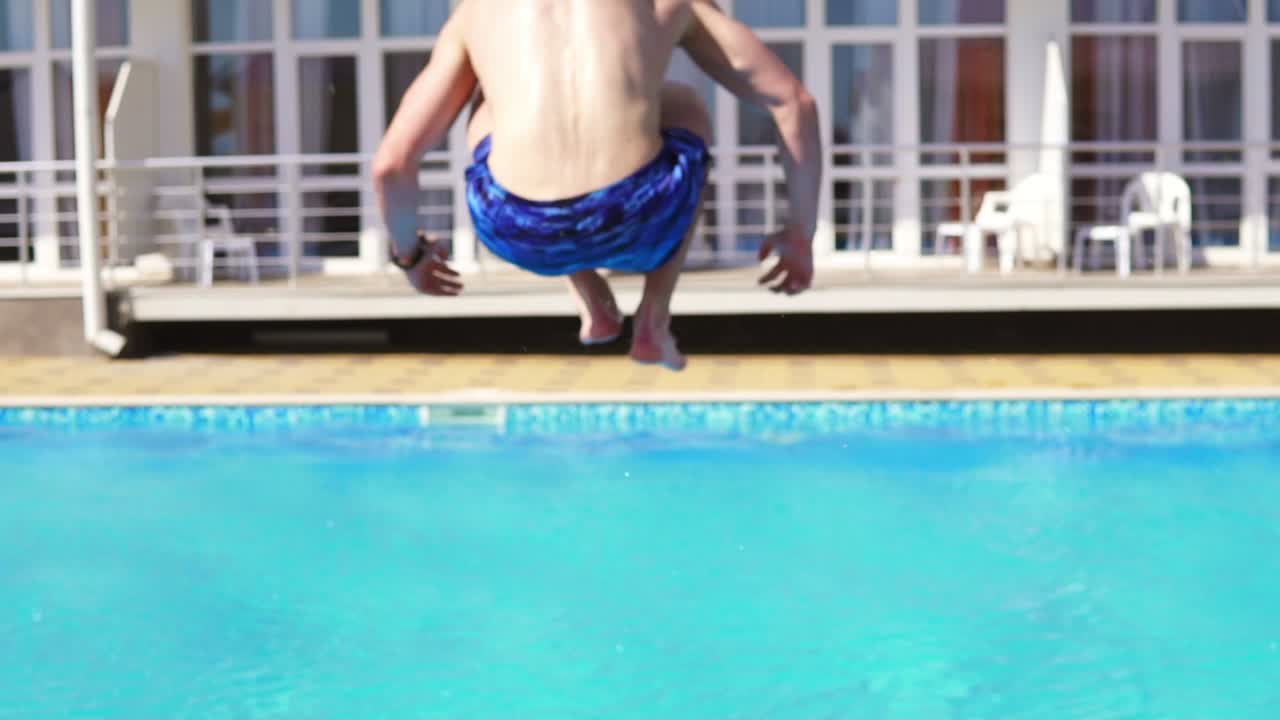 Back view of young athletic man in swim shorts running and jumping to the swimming pool. Slowmotion shot.