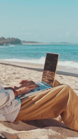 close up of hands of man freelancer typing on laptop sits on beach near sea
