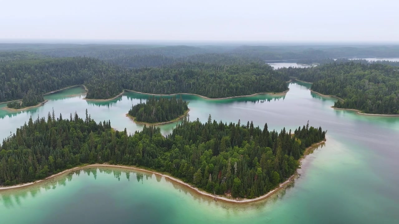 Luftfoto af en skovklædt ø med sandstrande omgivet af turkis og grønt vand ved Arnott Lake i det nordlige Ontario.