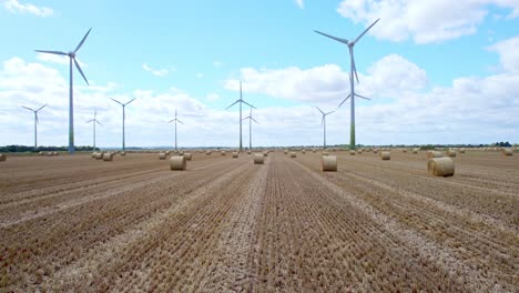 Captured-from-above,-a-row-of-wind-turbines-gracefully-turns-in-a-Lincolnshire-farmer's-freshly-harvested-field,-with-golden-hay-bales-in-the-foreground
