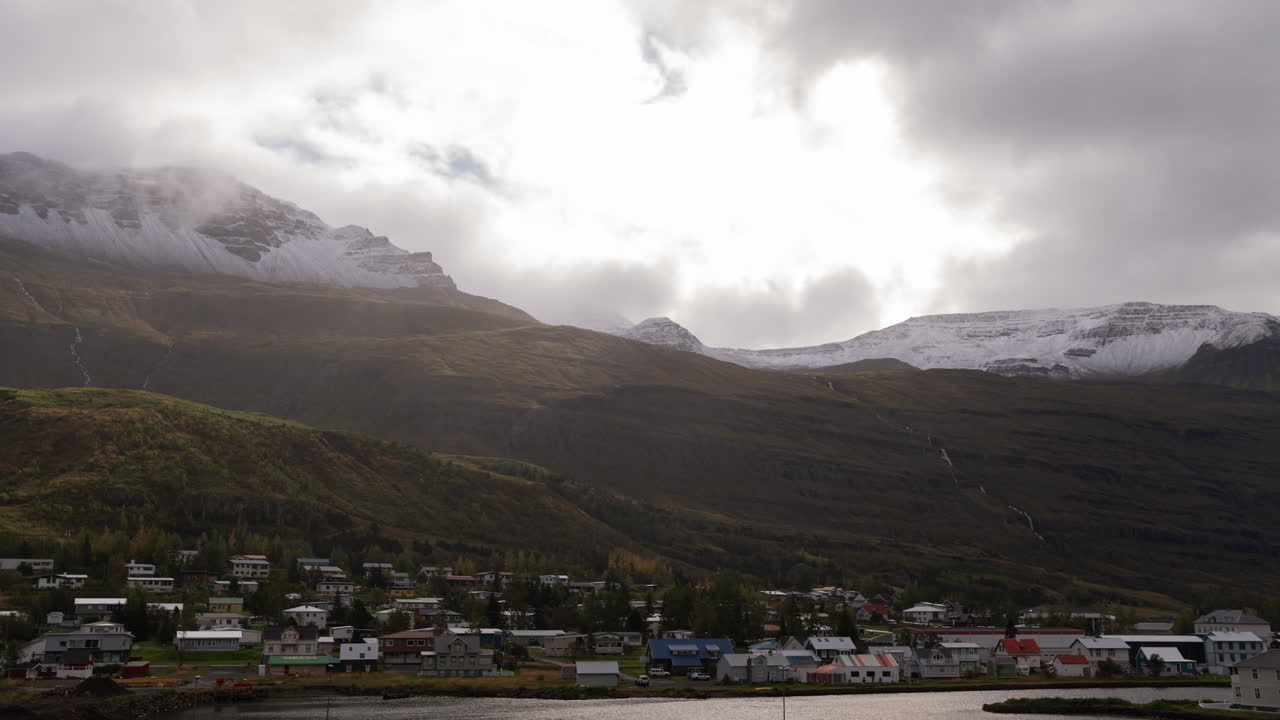 Timelapse van regen en mist boven het stadje Seyðisfjörður, IJsland, met lichtstralen die over de bergen vegen