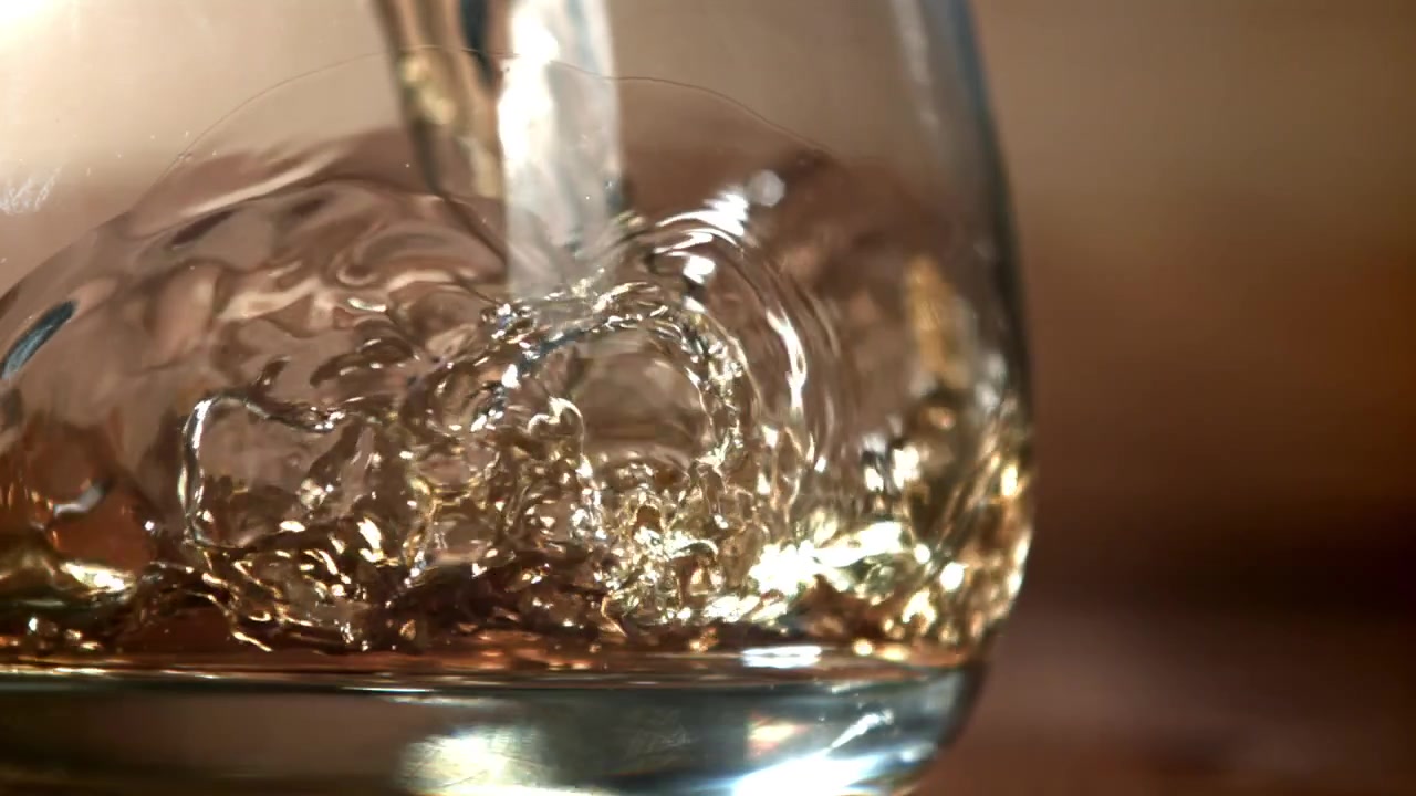 Primo piano al rallentatore di liquido ambrato dorato versato in un bicchiere
