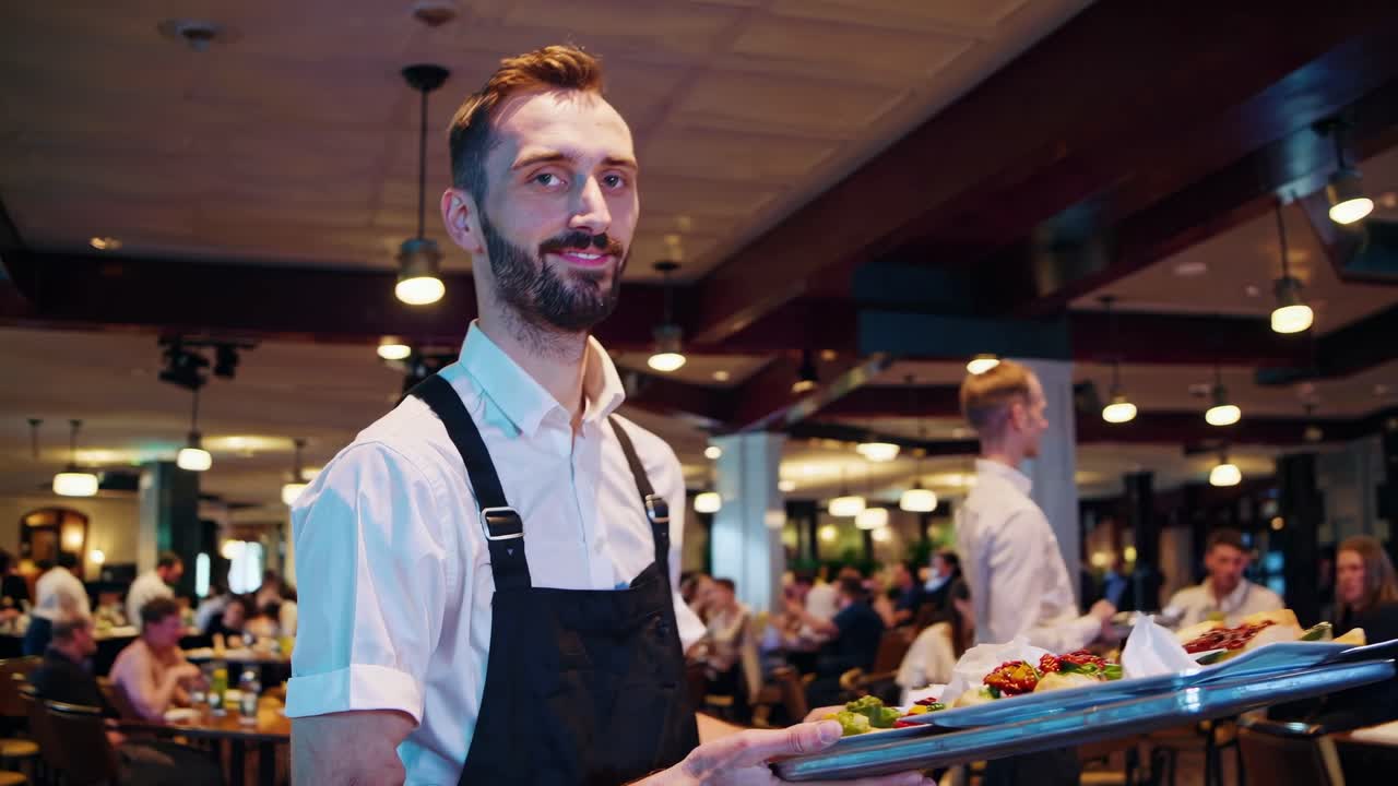 A waiter in a restaurant carrying a tray with food. The waiter is wearing a white shirt and black