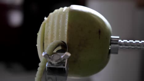 side view of metal kitchen device peeling, cutting and core green juicy apple skin and flesh on kitchen bench with juice flying out