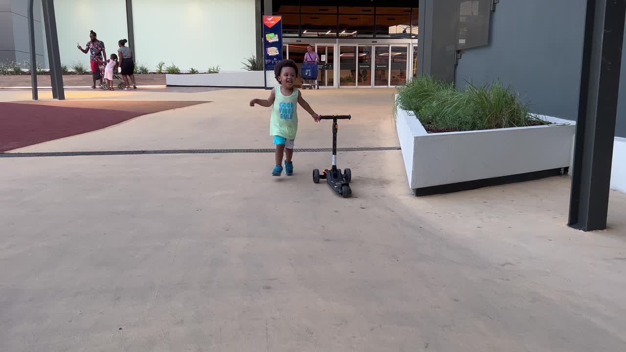 Two year old exotic and cute african europoean child playing happy with his first skateboard in a hot summer day, outdoor