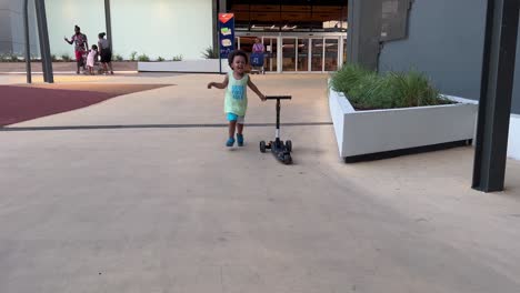 Niño-Europeo-Africano-Exótico-Y-Lindo-De-Dos-Años-Jugando-Feliz-Con-Su-Primera-Patineta-En-Un-Caluroso-Día-De-Verano,-Al-Aire-Libre