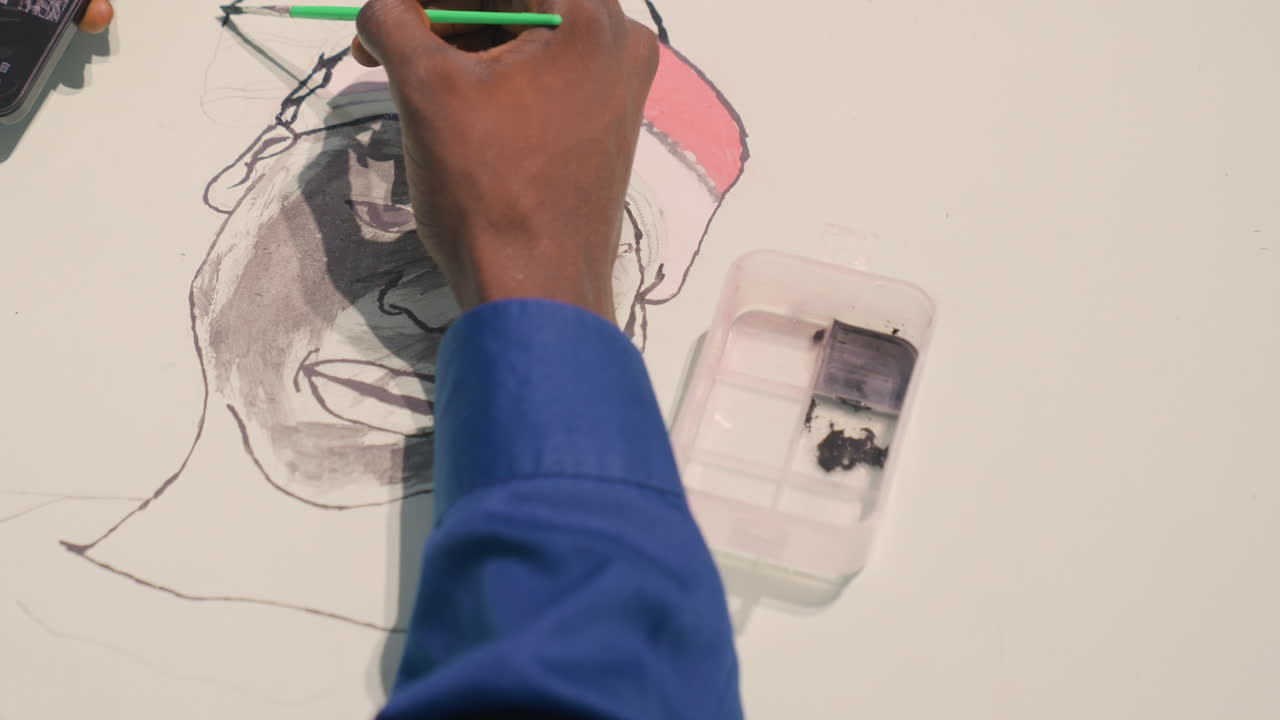 Black portrait underpainting artist hand painting slow gray wash builds facial form, pink hat rim outlined, blue sleeve visible, water tray and phone reference on table, soft studio light, focused