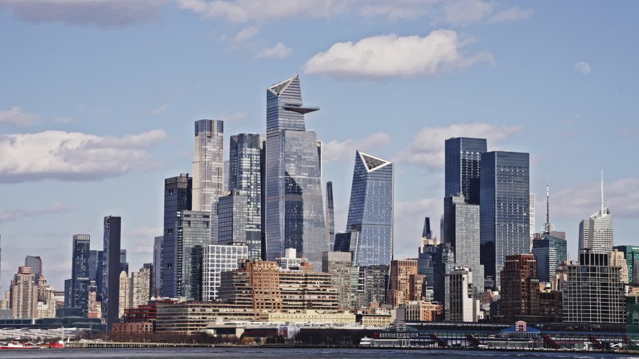 Panoramic view of Hudson Yards skyscrapers in Manhattan seen from across the Hudson River on a bright, partly cloudy day