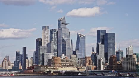 Panoramic view of Hudson Yards skyscrapers in Manhattan seen from across the Hudson River on a bright, partly cloudy day